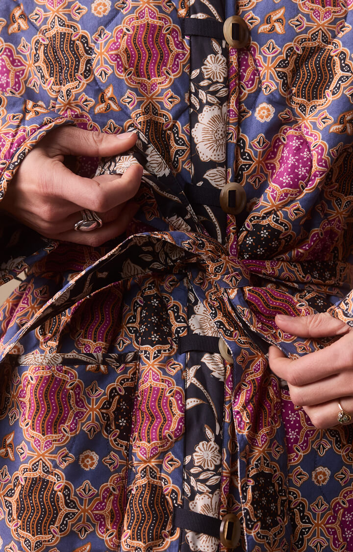 Close up image of model's hands tying waist belt of reversible quilted jacket